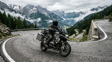 motorcyclist on winding mountain road with snow peaks
