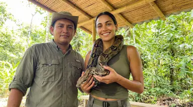 two people with boa constrictor in jungle
